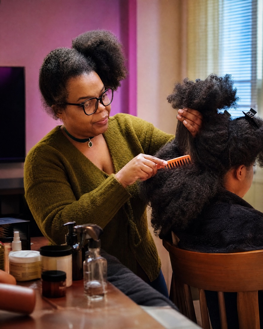 Kiki styling a woman's natural curly hair at her dining table